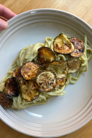 zucchini cream pasta with fried zucchini coins in a white bowl on a wooden countertop