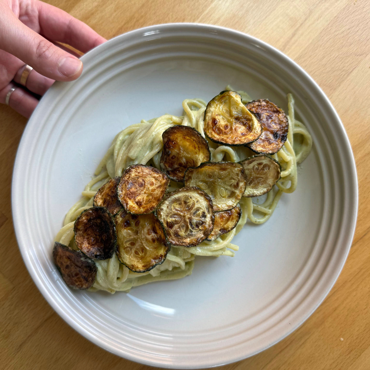 zucchini cream pasta with fried zucchini coins in a white bowl on a wooden countertop