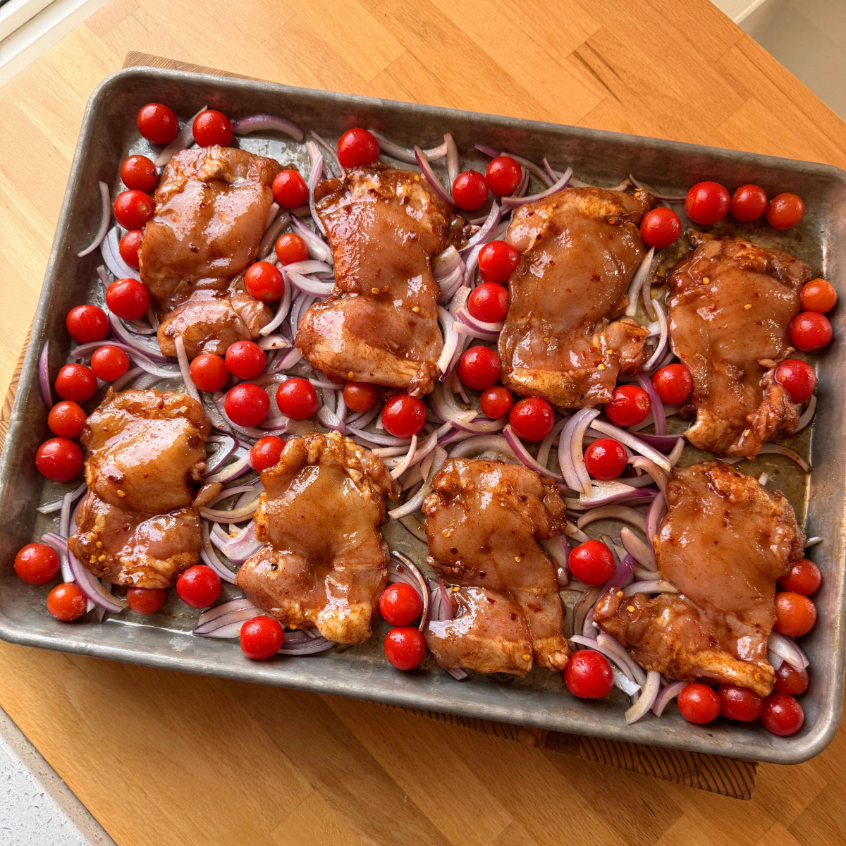 Boneless skinless chicken thighs, tomatoes and red onions on a sheet pan before going in the oven
