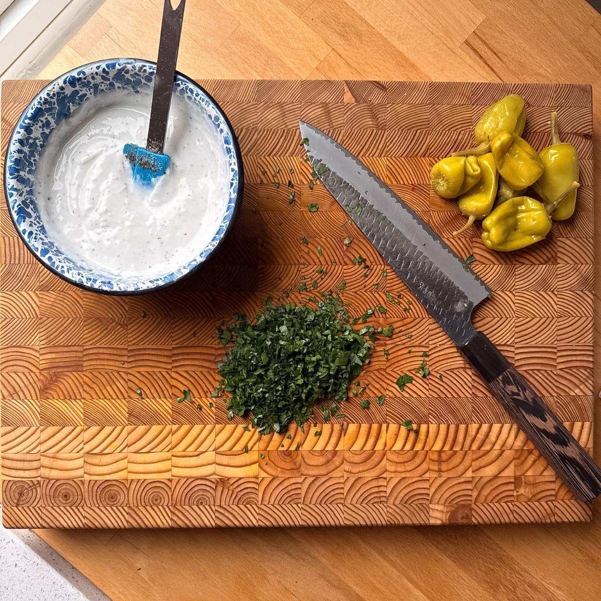 Garlic sauce, parsley and pepperoncini peppers on a cutting board ready to be served with sheet pan chicken shawarma