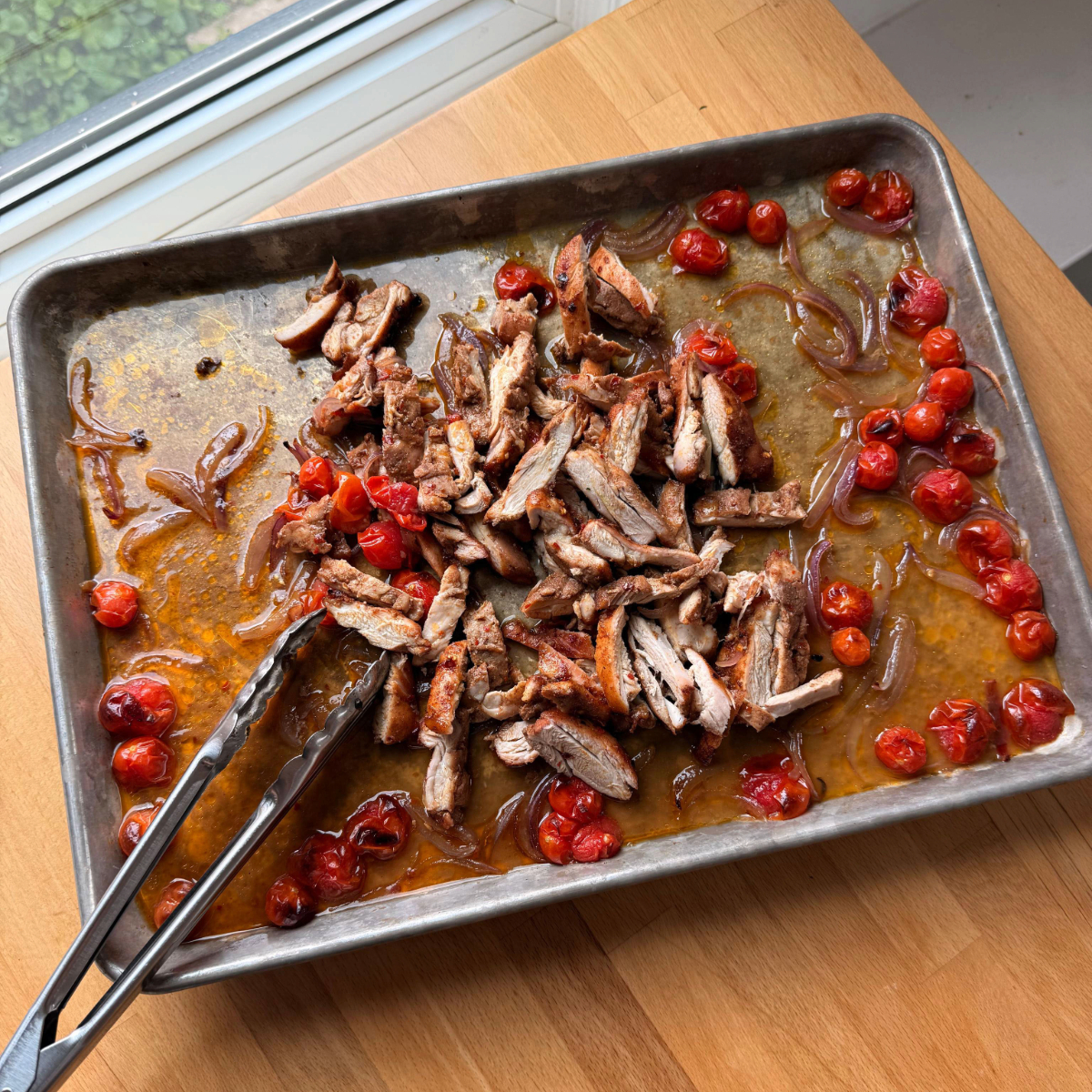 Sliced chicken thighs get transferred back to the sheet pan and tossed in remaining pan sauce