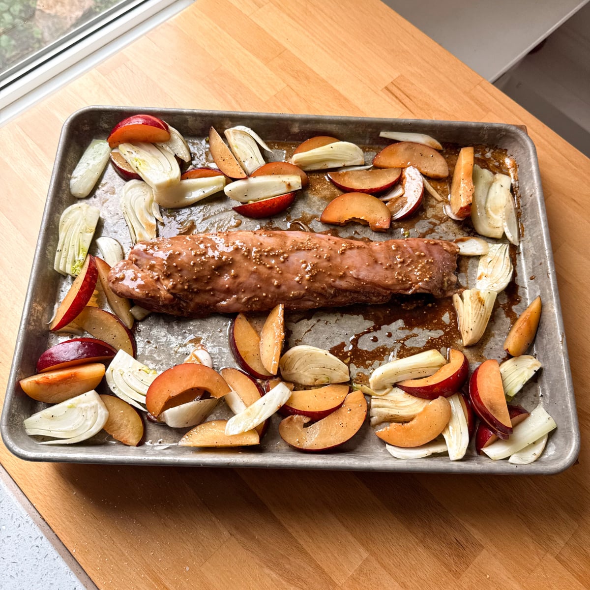pork tenderloin on a sheet pan with plums, fennel and seasoning ready to be roasted in the oven