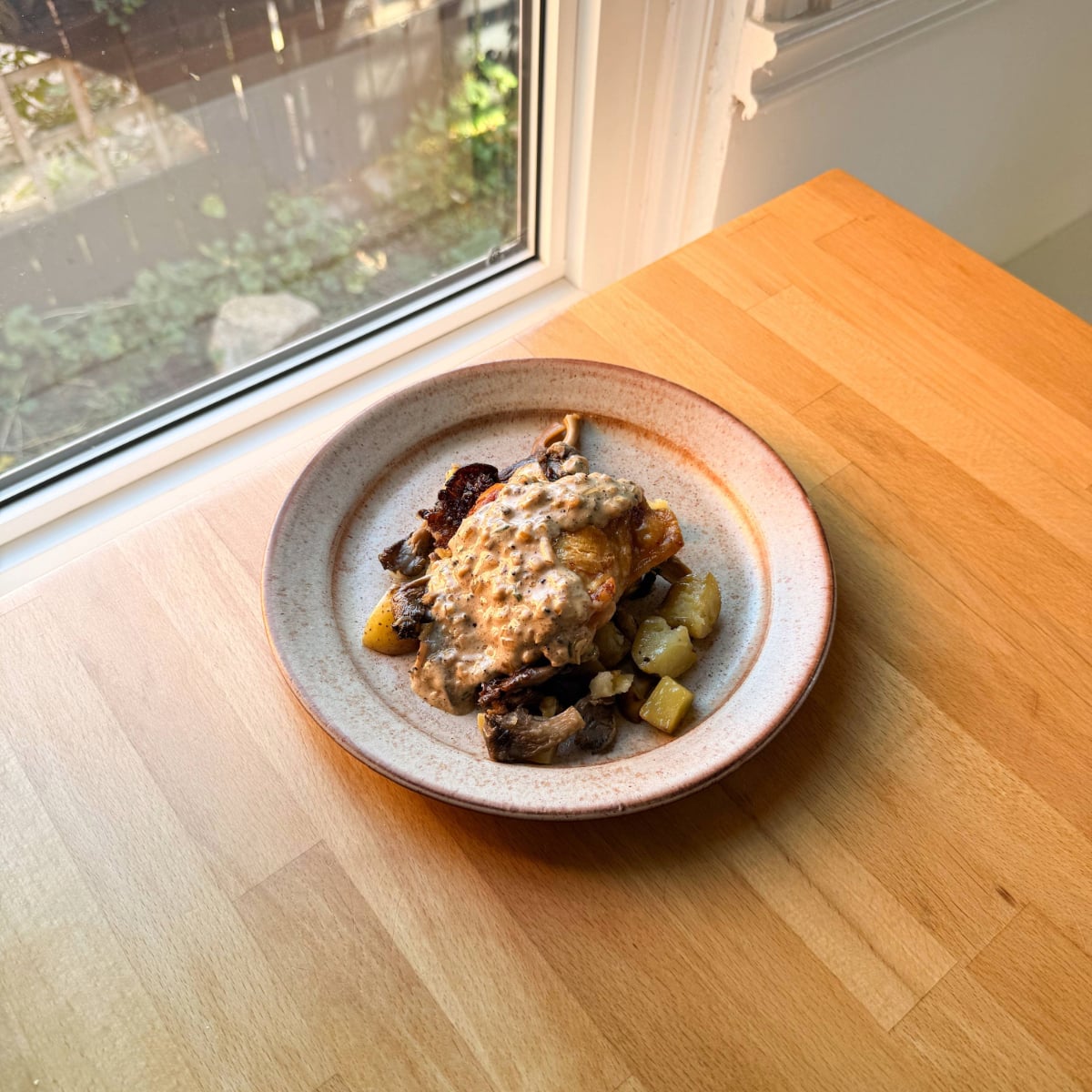 an oven baked chicken thigh sits on a plate with potatoes and mushrooms topped with pepper sauce