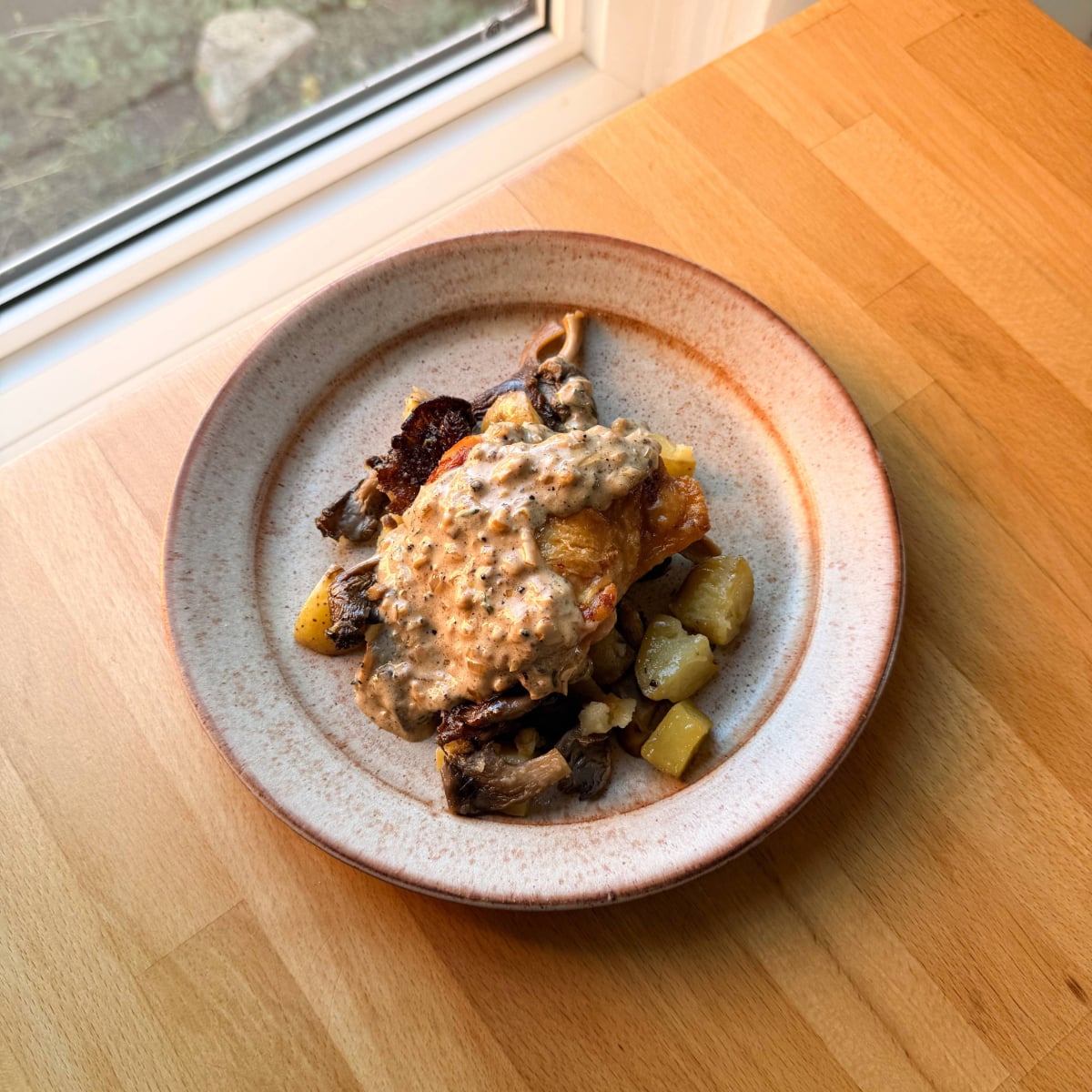 an oven baked chicken thigh on a plate with potatoes and mushrooms topped with au poivre sauce