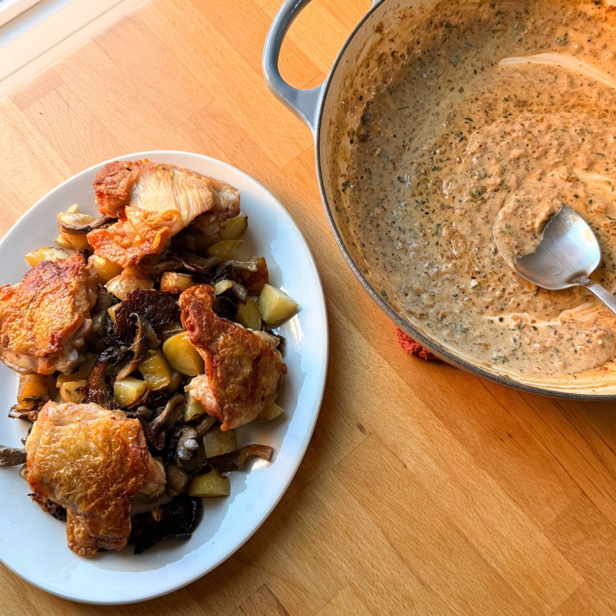 a plate of crispy skin chicken thighs with potatoes, mushrooms beside a pot of au poivre sauce