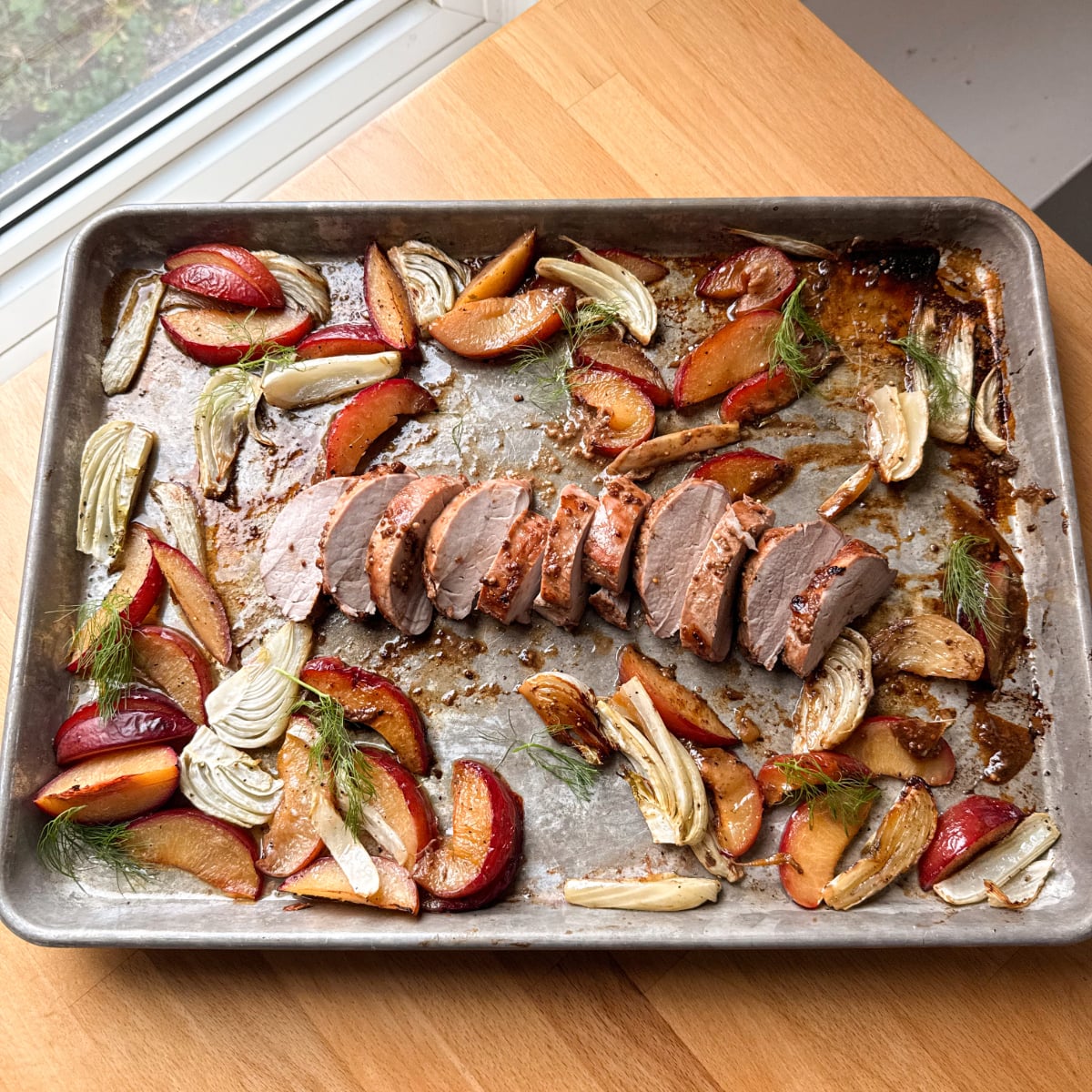 Sliced pork tenderloin with roasted plums and fennel on a sheet pan